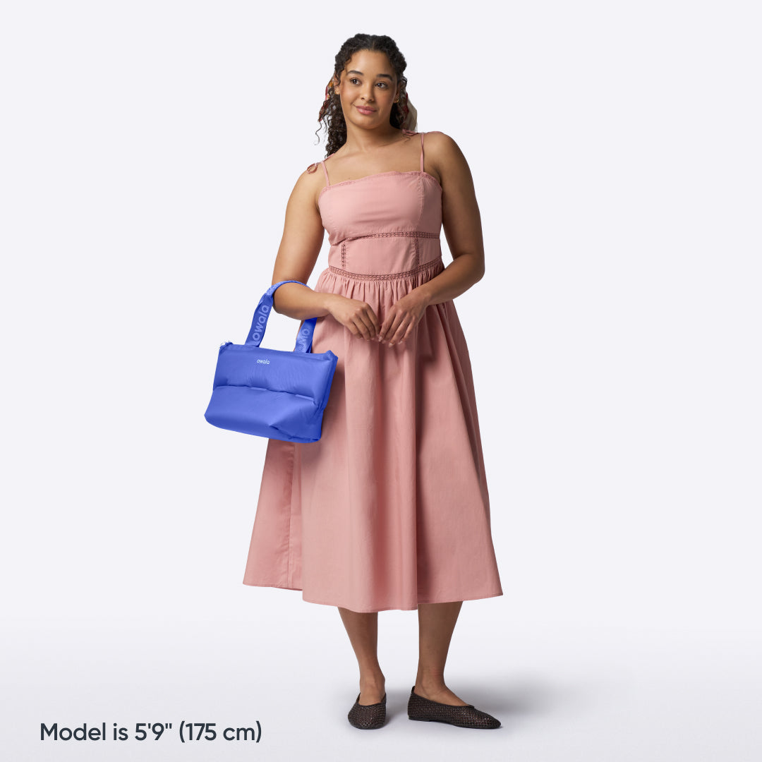 Owala Puffer Mini in Al Fresco, cobalt blue puffy tote held in the hand of a woman in a pink dress, with text reading "Model is 5'9" (175 cm)"